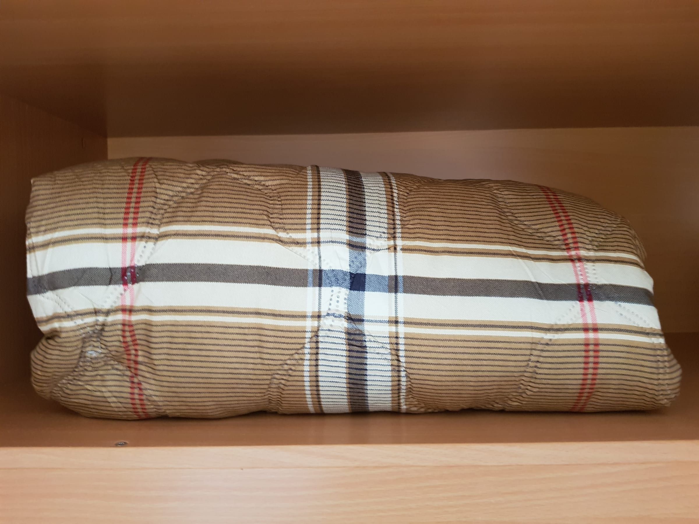 Gefaltete Steppdecke mit beige-braunem Karomuster im Schrank