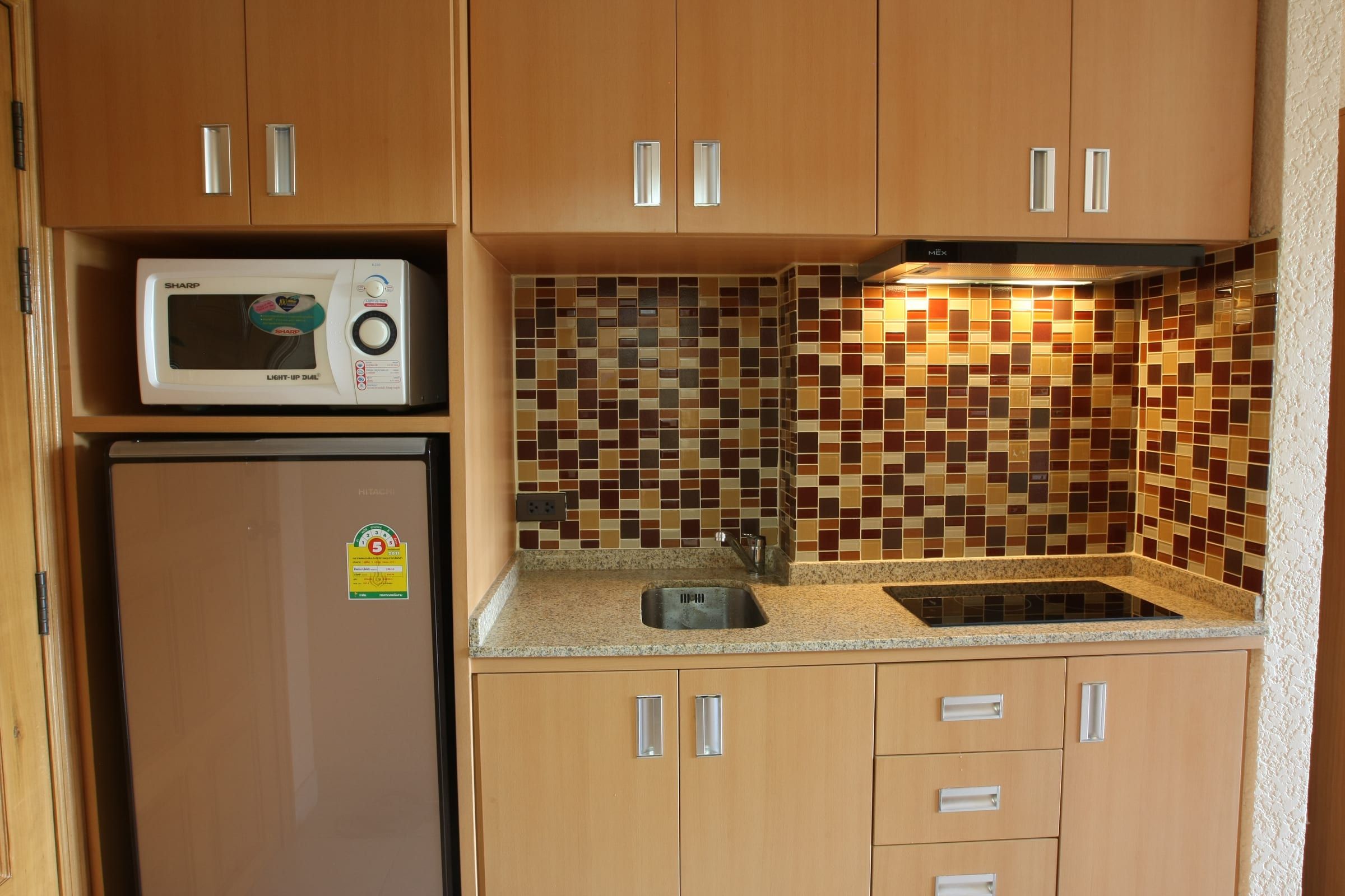 Einbauküche Typ A mit hellen Holzfronten, Mosaikfliesen, Mikrowelle, Kühlschrank und Ceranfeld