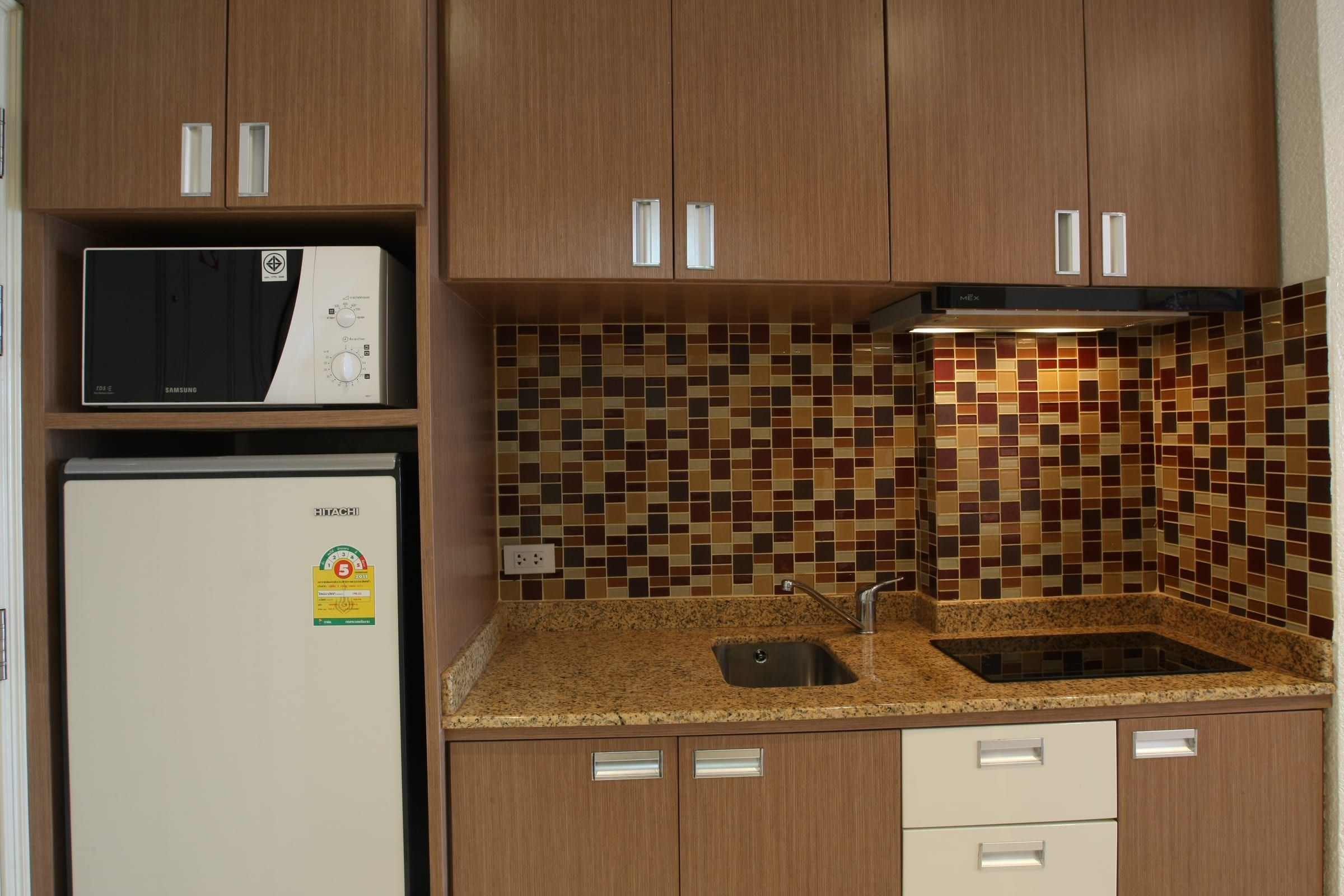 Einbauküche Typ B mit dunkleren Holzfronten, Mosaikfliesen, Mikrowelle und Kühlschrank