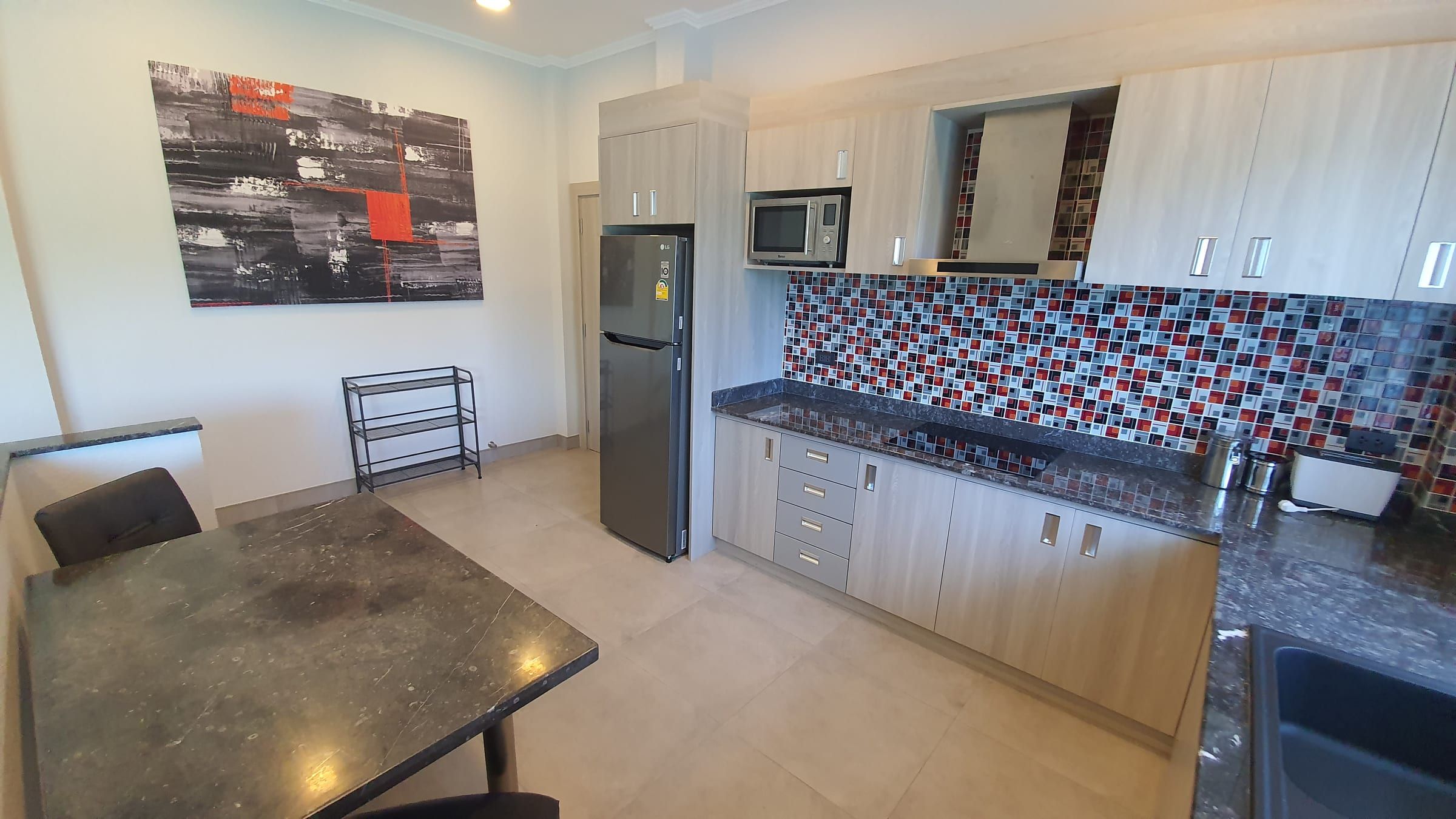 Coin repas avec table en pierre foncée et cuisine équipée avec mosaïque et réfrigérateur