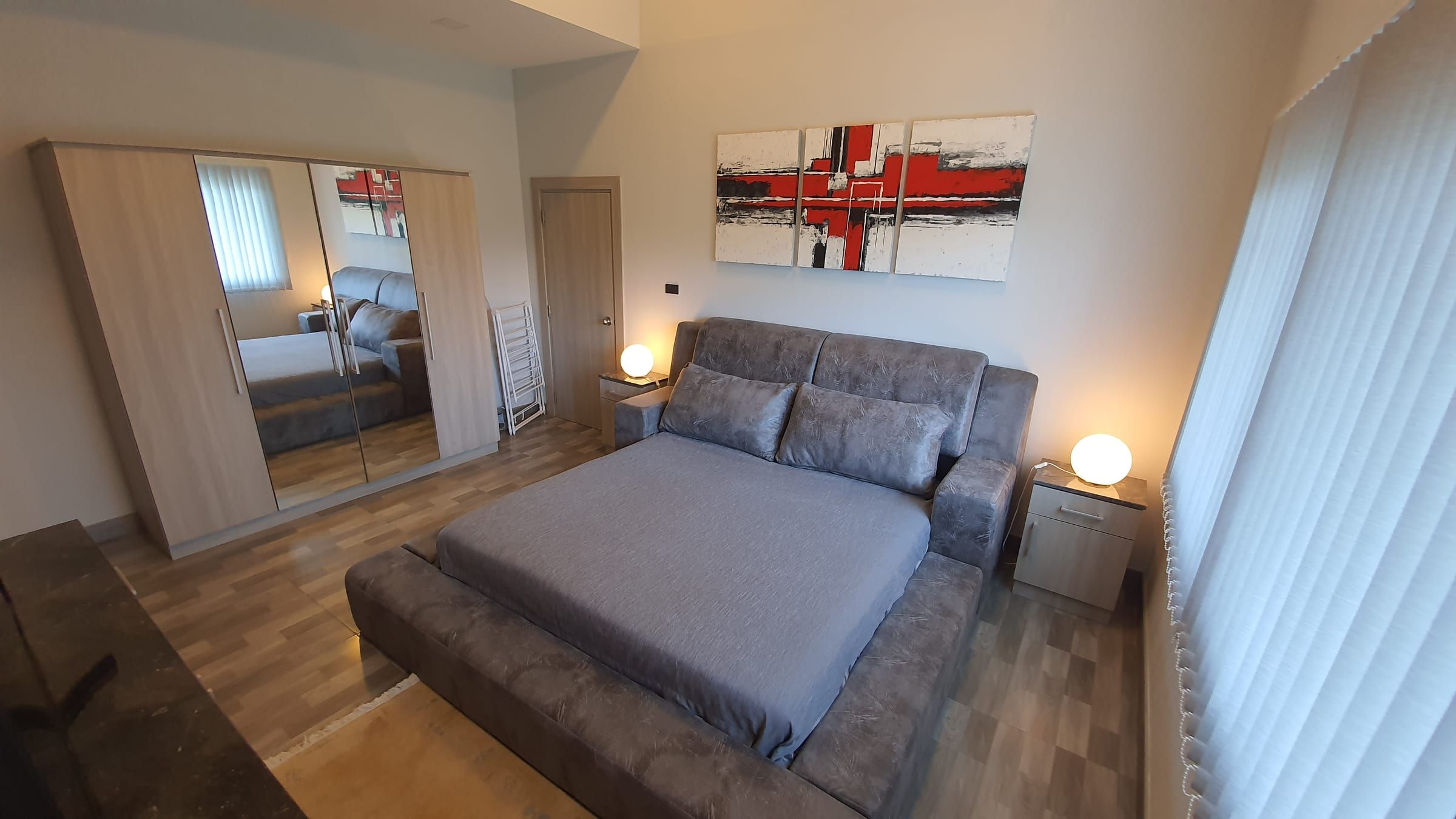 Chambre avec lit double gris, armoire à miroirs et tableau rouge et blanc