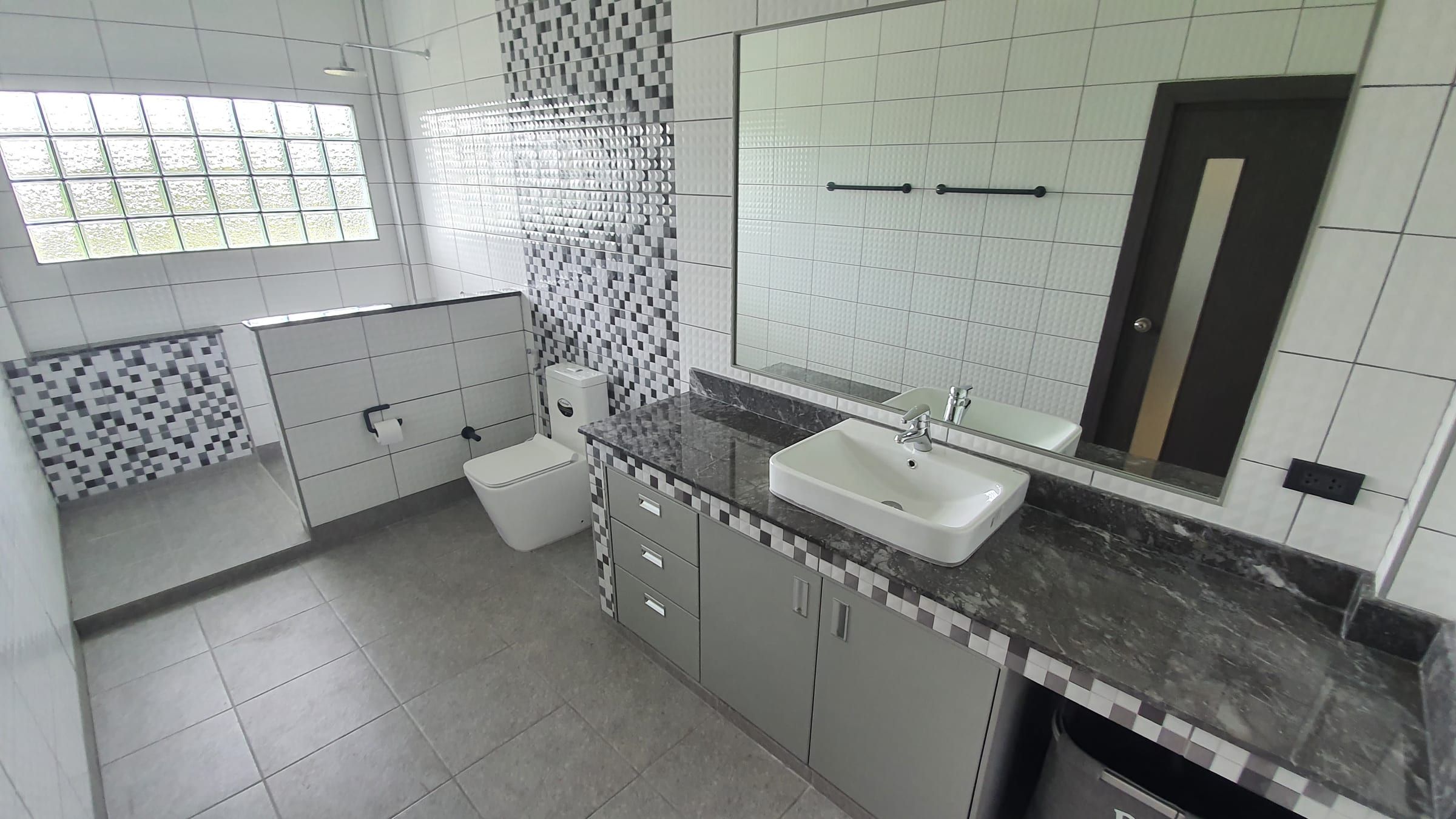 Salle de bains au carrelage gris, vasque sur plan en pierre foncée et espace douche