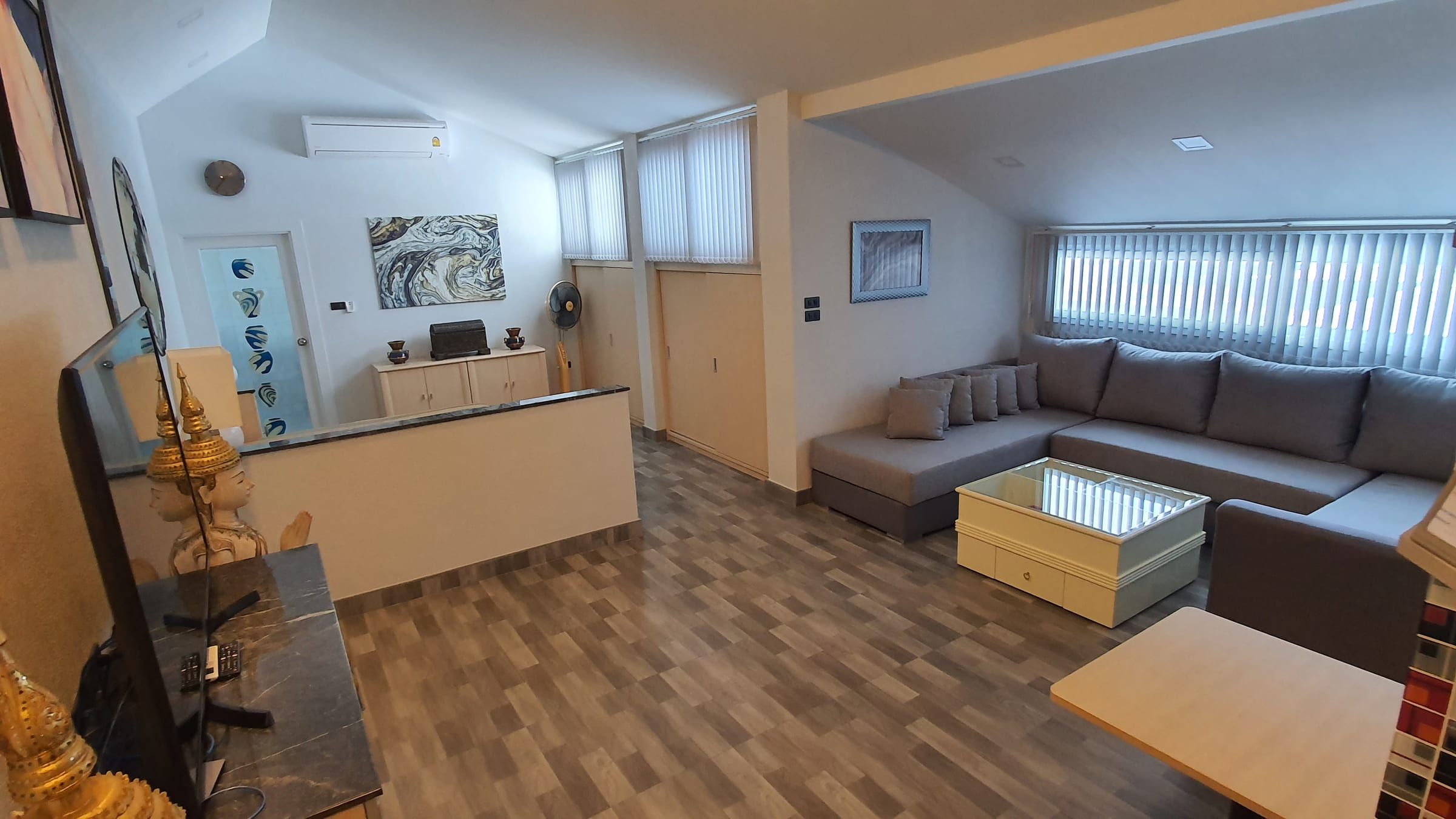 Espace de vie avec canapé d'angle gris, comptoir de cuisine et parquet