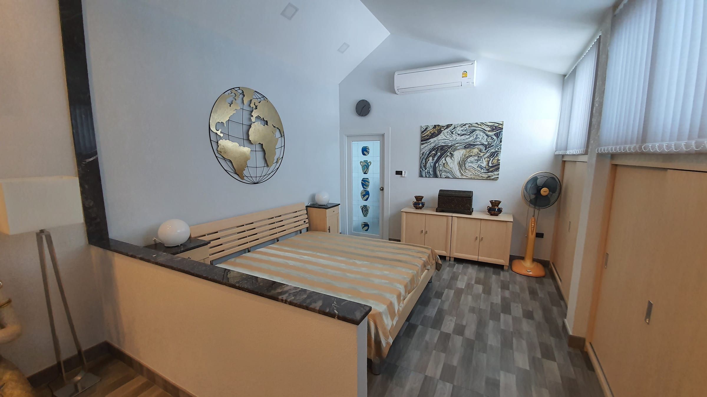 Chambre avec lit, carte du monde au mur, ventilateur et armoire