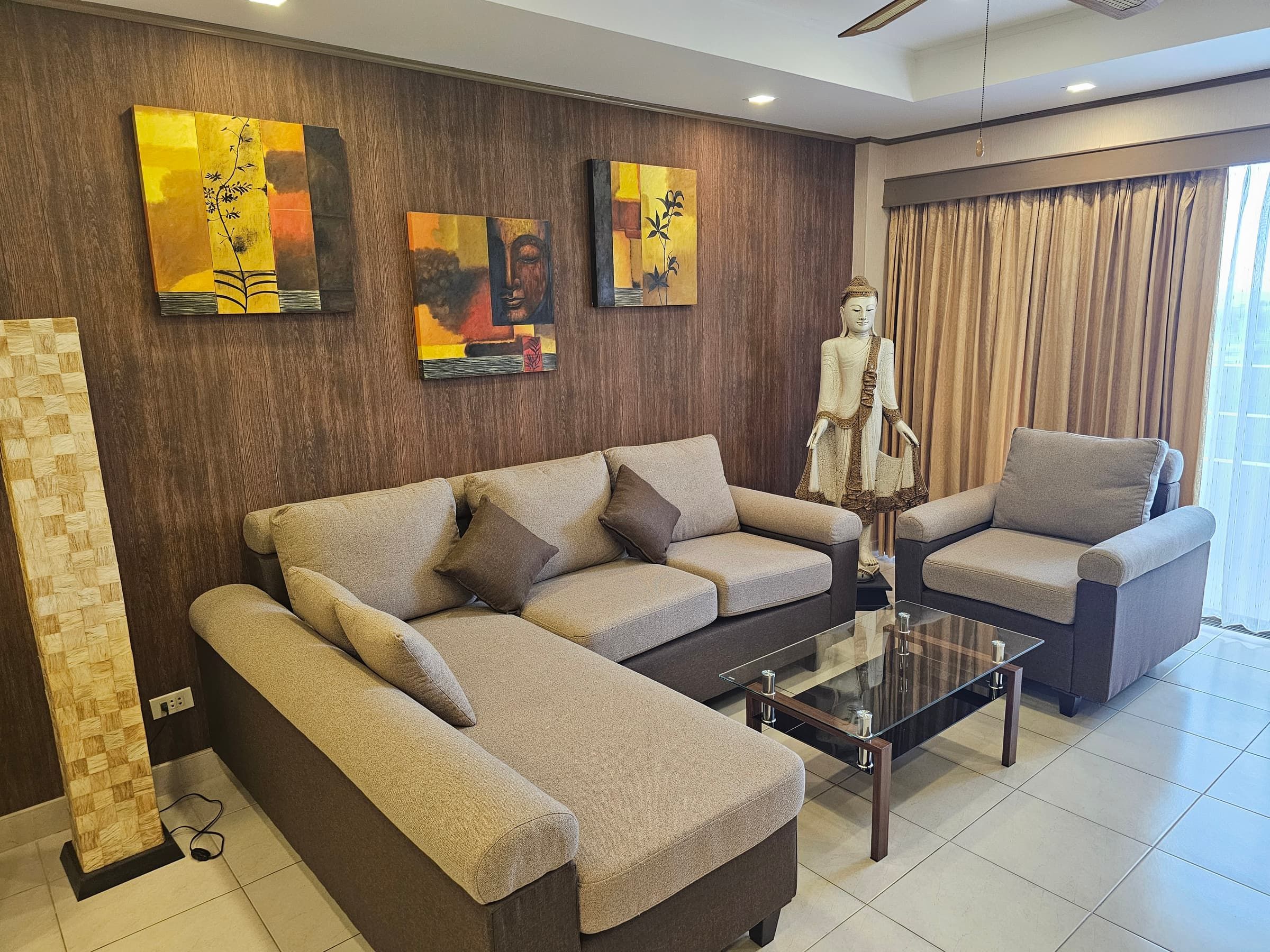 Beige sofa suite with a glass table, pictures on the wall and a Buddha figure