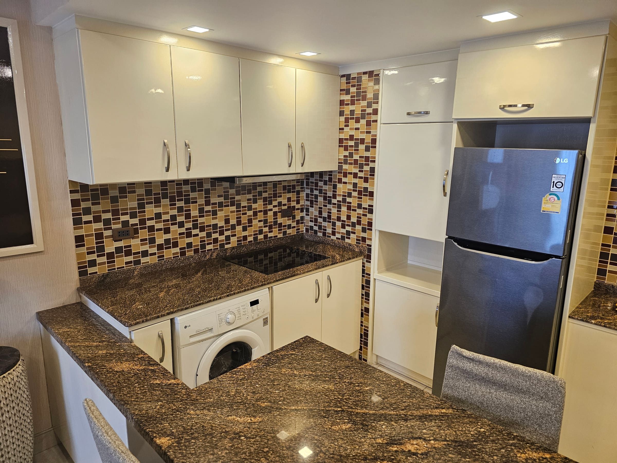 Fitted kitchen with white fronts, granite worktop, mosaic tiles, washing machine and fridge-freezer