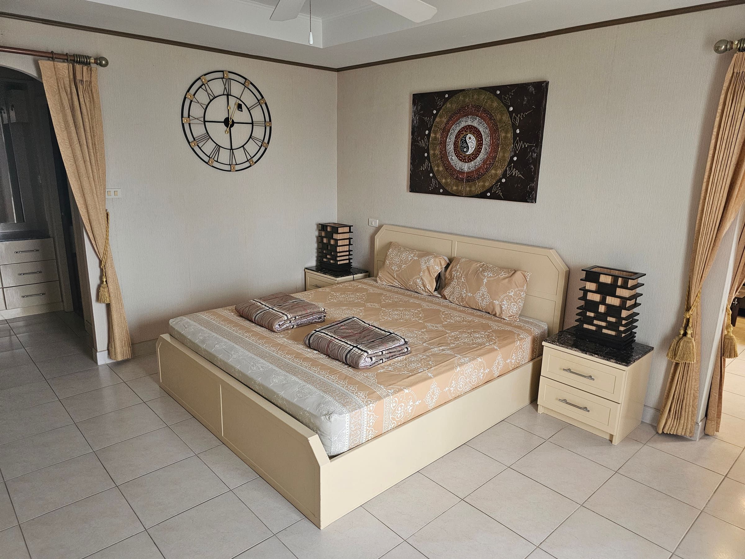Bedroom with king-size bed, beige bedspread, bedside tables, wall clock and mandala picture