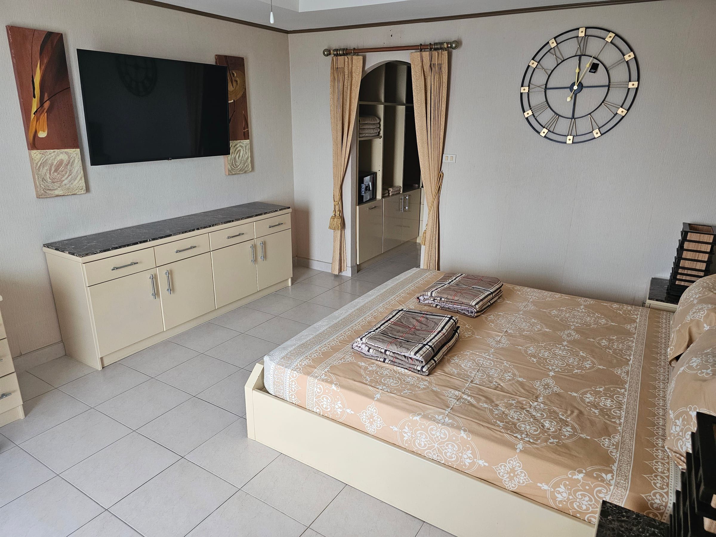 Bedroom with wall-mounted flat-screen TV, sideboard and a bed with a patterned bedspread