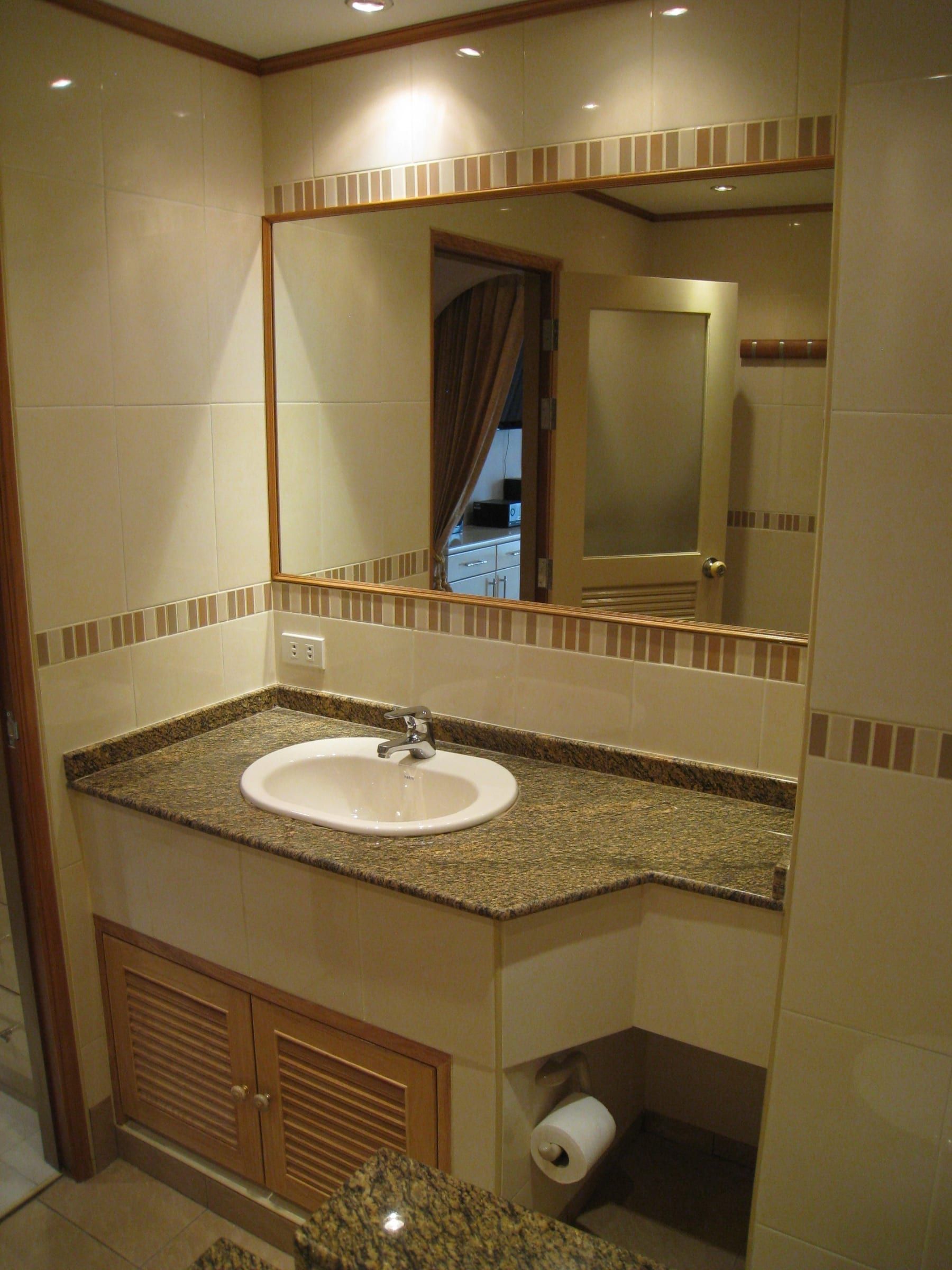 Bathroom with washbasin on a granite counter, large mirror and wooden cabinet