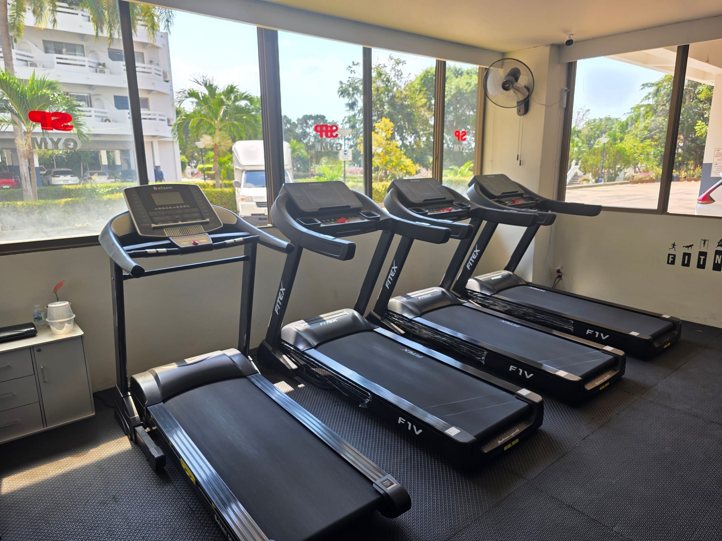 Vier Laufbänder in einer Reihe vor den Fenstern des Fitnessstudios