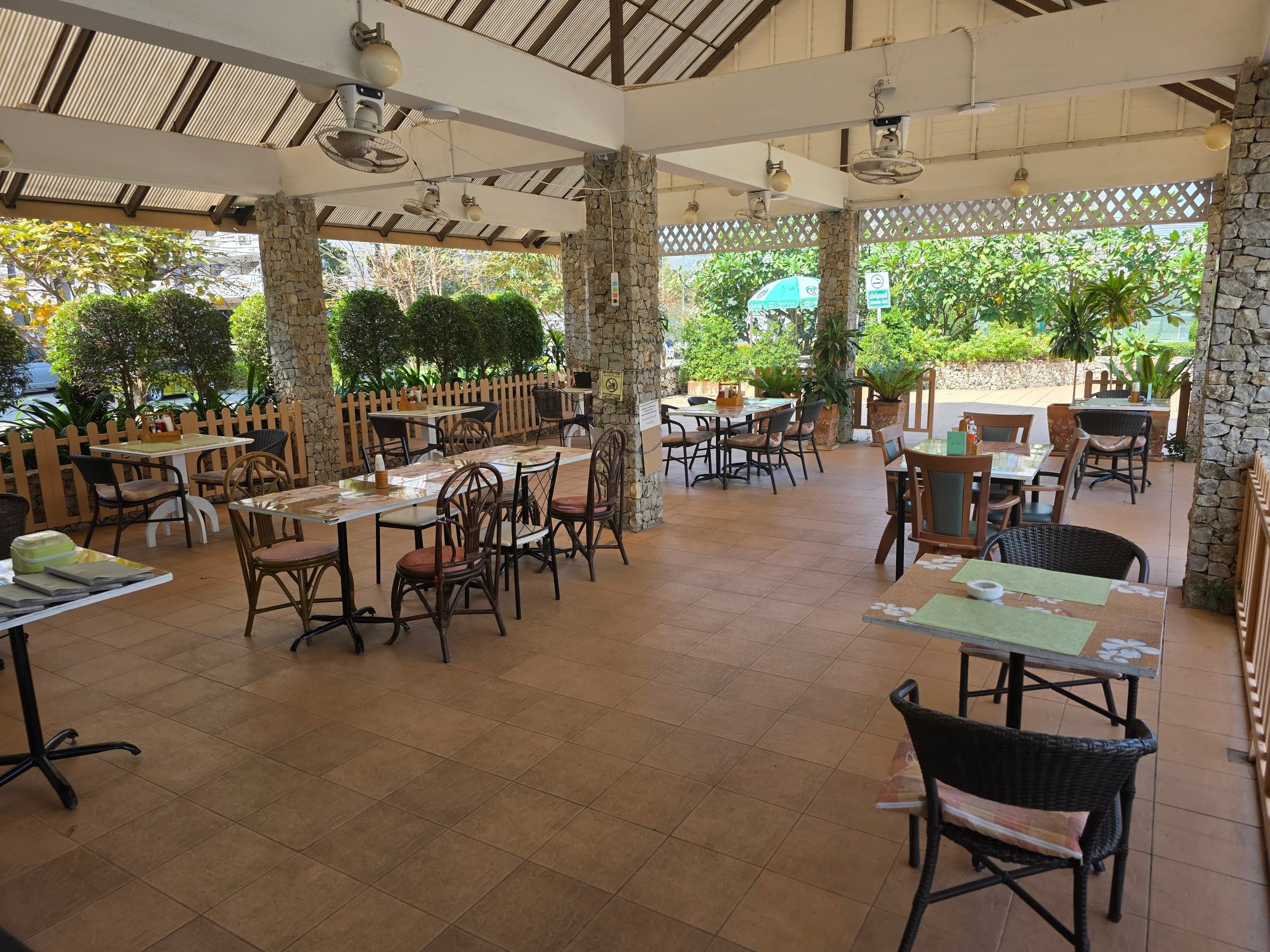 Überdachte Terrasse des Pool-Restaurants mit gedeckten Tischen, Stühlen und Blick in den Garten