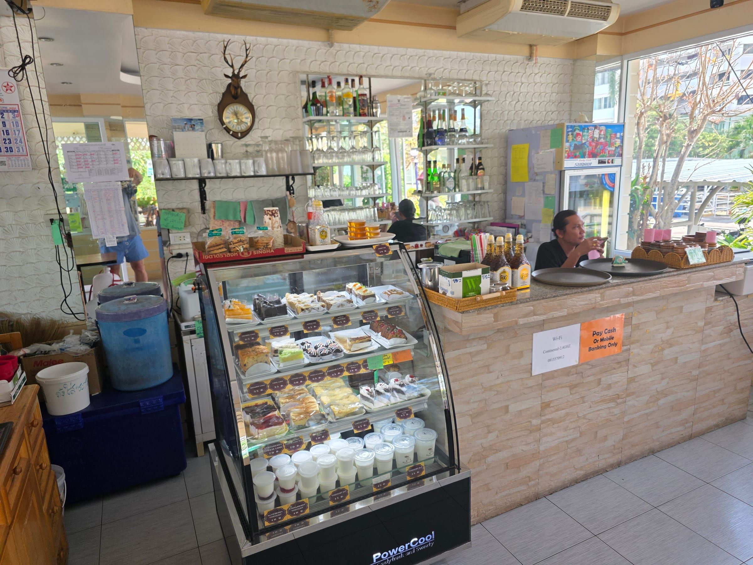 Tresen des Restaurants mit Kuchenvitrine, Getränkeregal und Wanduhr