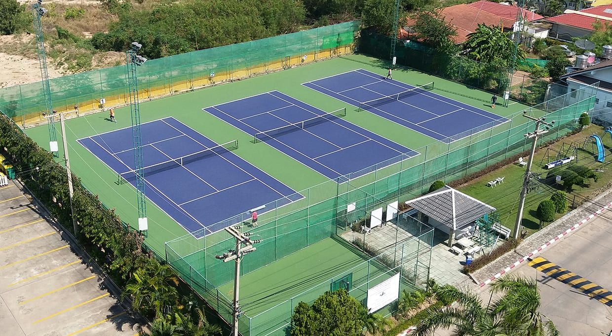 Aerial view of the three blue tennis courts with green surroundings and floodlight masts