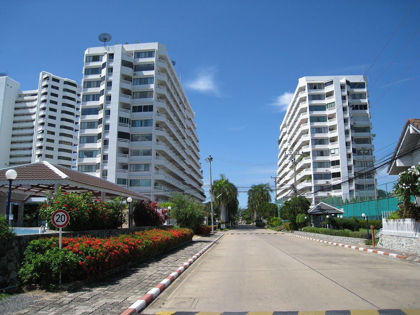 Die beiden weißen Wohntürme von Jomtien Condotel mit der Zufahrtsstraße und Blumenbeeten unter blauem Himmel